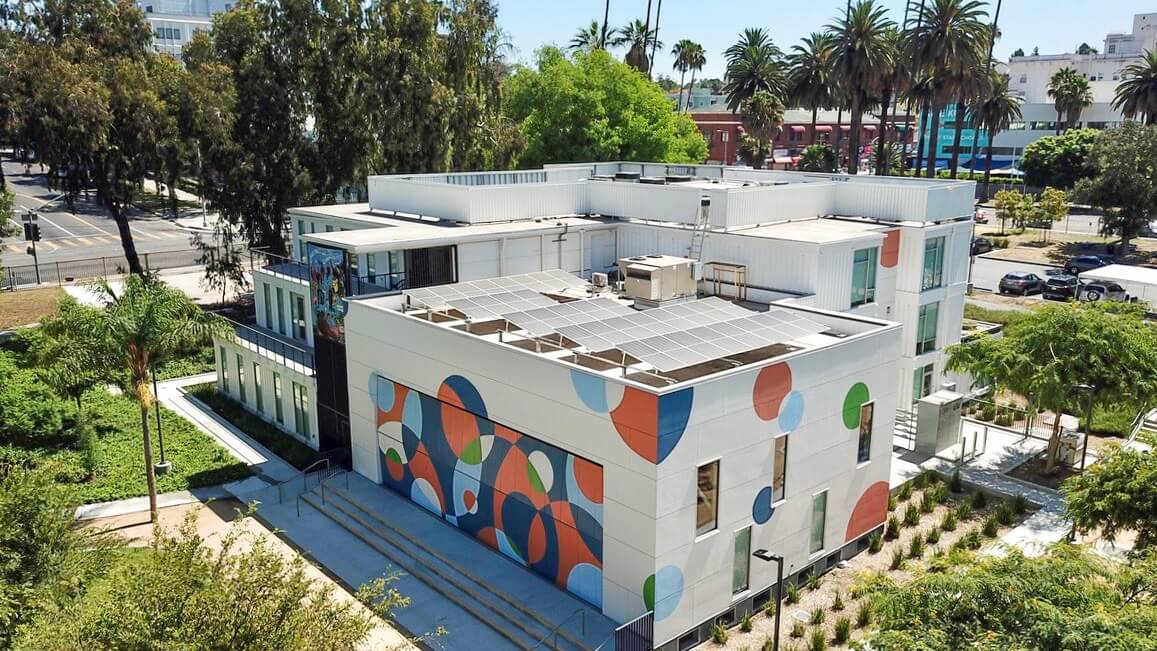 Modern building with rooftop solar panels and a colorful geometric mural in an urban setting