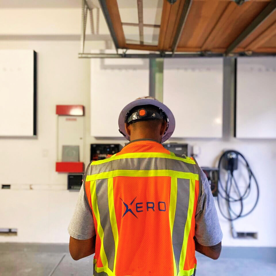 Xero technician in a safety vest inspecting a solar battery storage