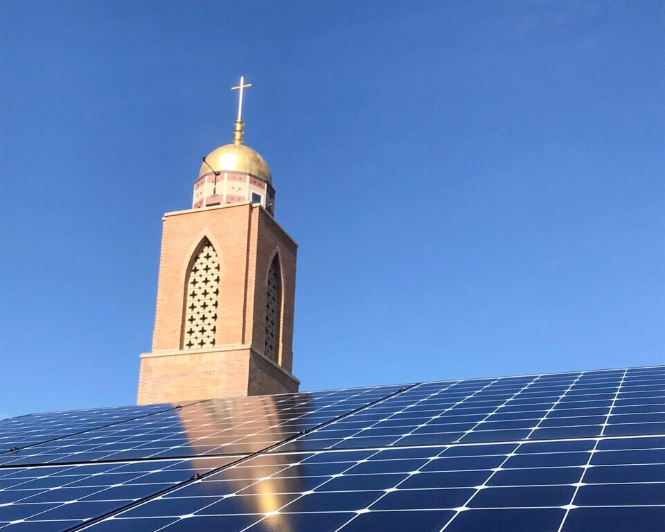 Solar panels reflecting sunlight with a church tower and blue sky in the background